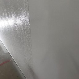 Firma MALOREM - Świeżo nałożona, mokra warstwa gładzi na ścianie, kontrastująca z suchą, gładką powierzchnią obok, widok z dołu ukazujący przejście między strukturami.