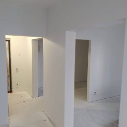 Firma MALOREM - Wnętrze po świeżym pomalowaniu na biało, widoczne przejścia między pomieszczeniami, zabezpieczona folią podłoga i ślady po gniazdkach elektrycznych.