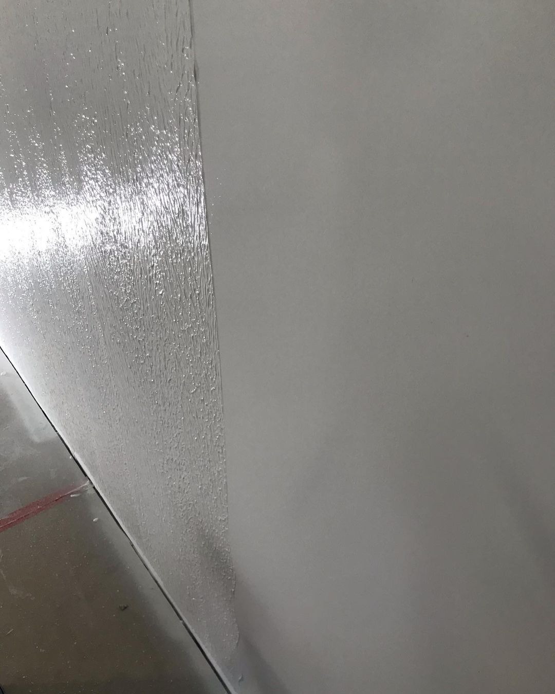 Świeżo nałożona, mokra warstwa gładzi na ścianie, kontrastująca z suchą, gładką powierzchnią obok, widok z dołu ukazujący przejście między strukturami.