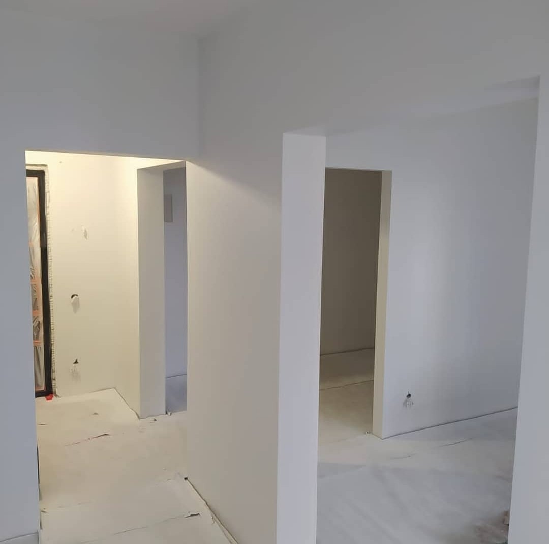 Wnętrze po świeżym pomalowaniu na biało, widoczne przejścia między pomieszczeniami, zabezpieczona folią podłoga i ślady po gniazdkach elektrycznych.