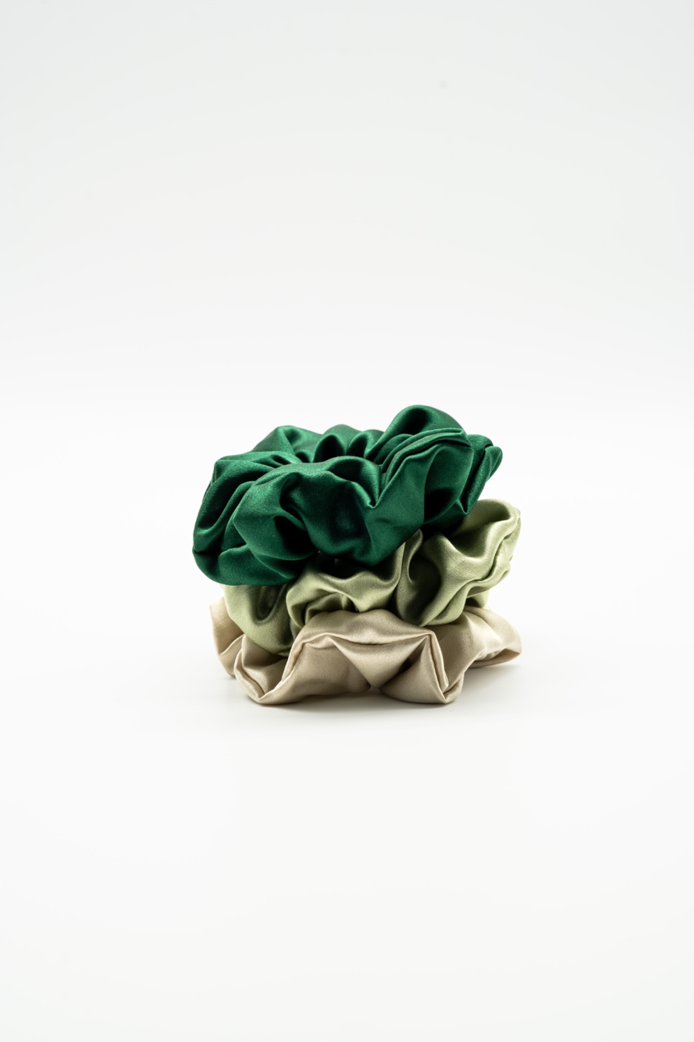 Stos trzech satynowych gumek do włosów w odcieniach zieleni i beżu, na białym tle, wykonanych w Lubinie.