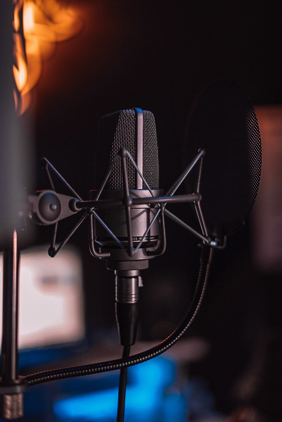 Studyjny mikrofon pojemnościowy z pop filtrem na tle ciemnego pomieszczenia z rozproszonym światłem