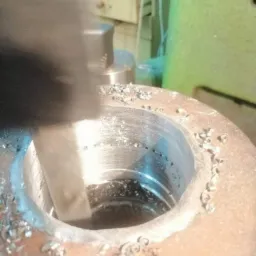 Metalowy element obrabiany tokarką, widoczne wióry i narzędzie w trakcie pracy.