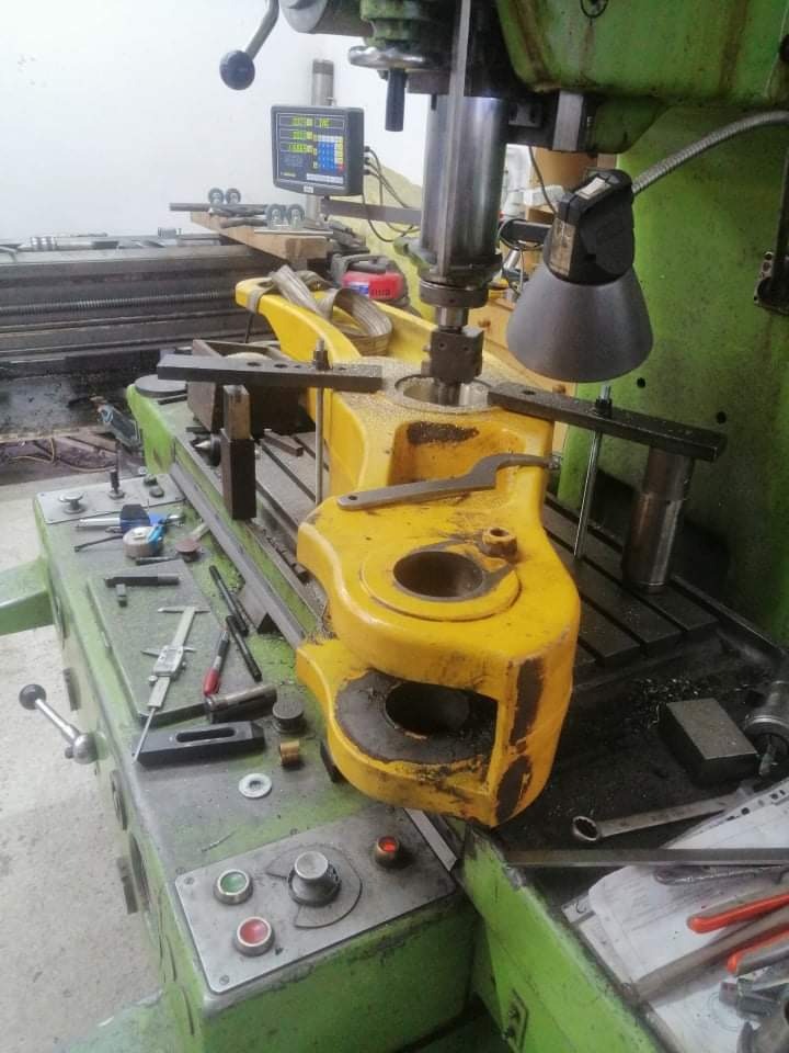 Żółty element obrabiany na frezarce CNC, widoczne wióry, narzędzia pomiarowe i sterownik numeryczny.