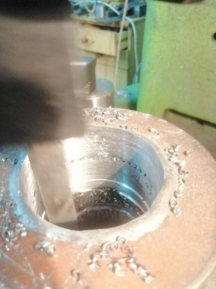 Metalowy element obrabiany tokarką, widoczne wióry i narzędzie w trakcie pracy.