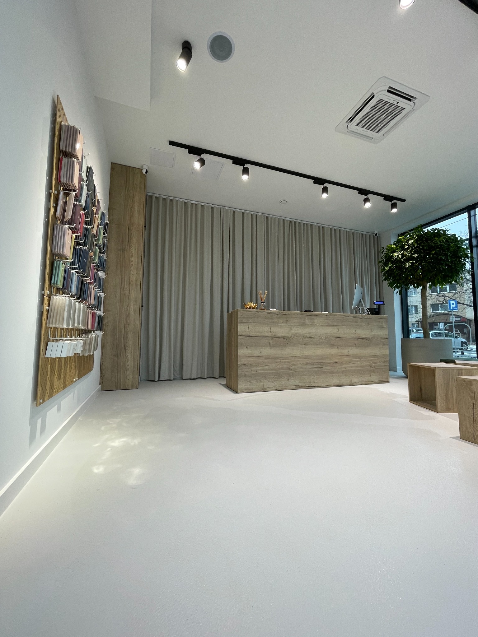 Nowoczesne wnętrze sklepu z minimalistyczną ladą recepcyjną z drewnopodobnego materiału, widoczne oświetlenie szynowe, klimatyzacja kasetonowa i ekspozycja akcesoriów na ścianie.