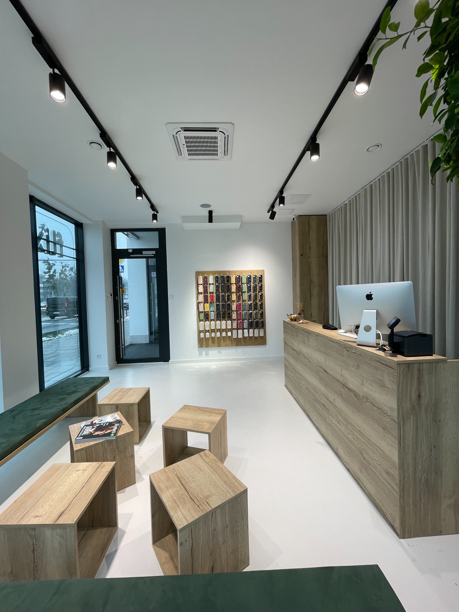 Jasne wnętrze sklepu z akcesoriami do telefonów, widoczny blat obsługi z komputerem Apple, ekspozycja etui na ścianie, minimalistyczne meble i oświetlenie punktowe.