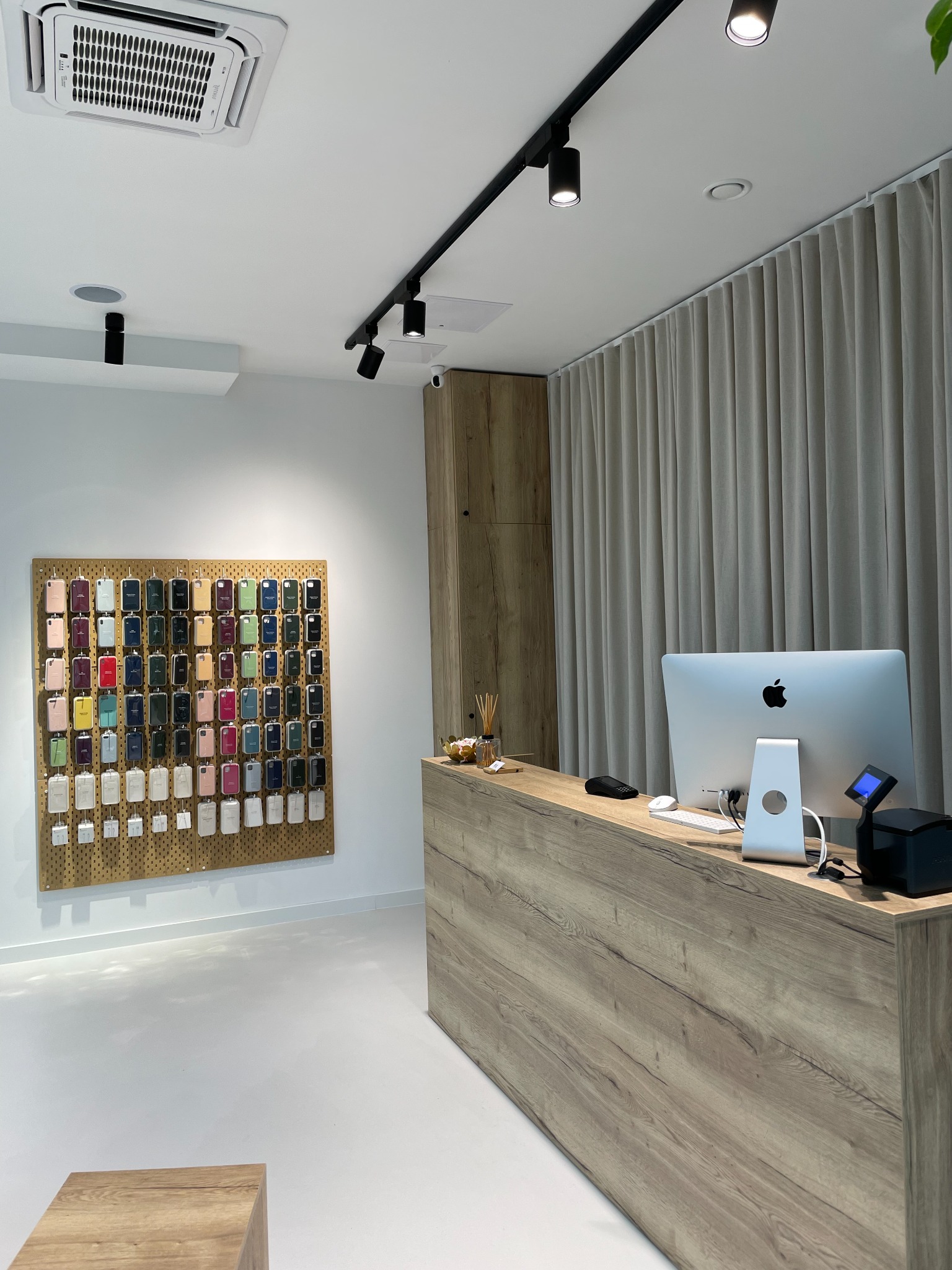 Wnętrze sklepu z akcesoriami do telefonów: drewniana lada recepcyjna z komputerem iMac, na ścianie ekspozycja etui na telefony w różnych kolorach.