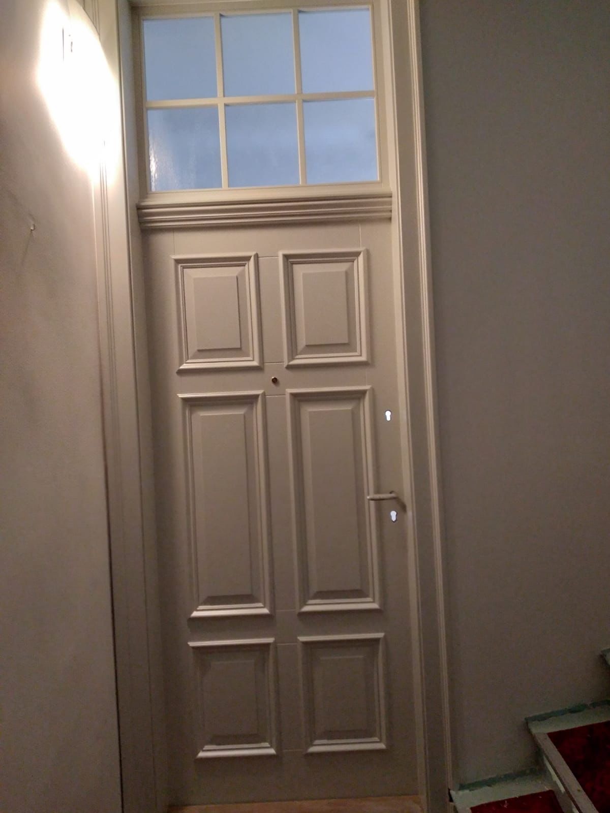 Białe, klasyczne drzwi wewnętrzne z górnym świetlikiem, widoczne na klatce schodowej.