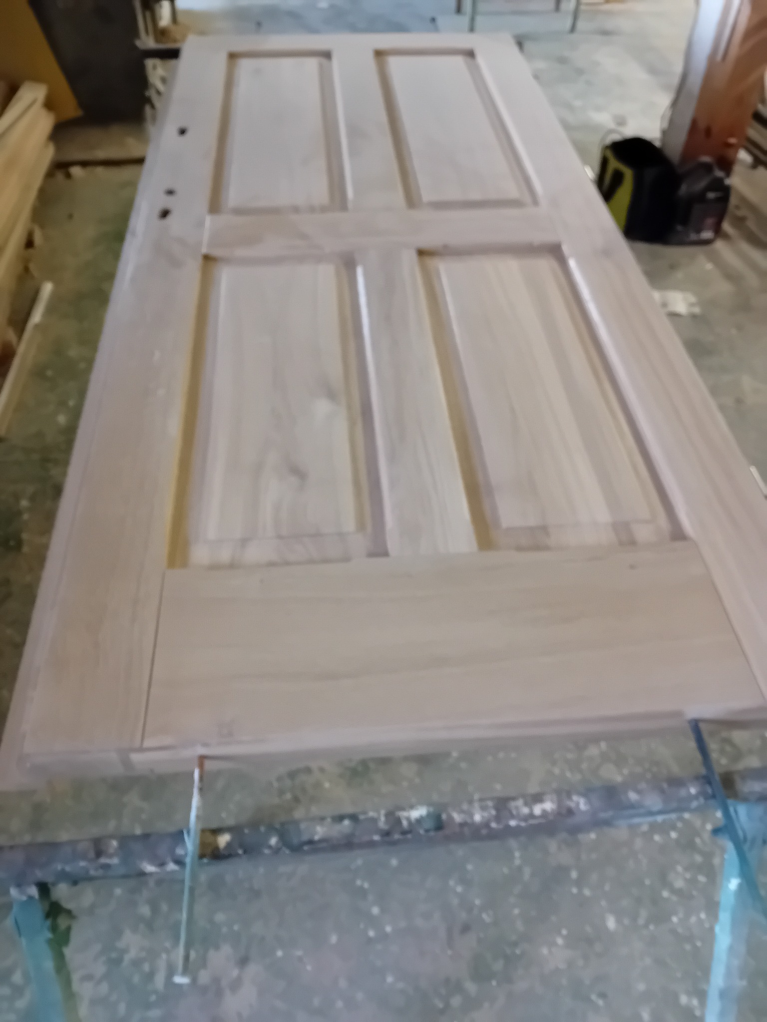 Surowa drewniana rama drzwi z czterema panelami, leżąca na roboczym stole, widoczne otwory na klamkę i zamek, przygotowana do dalszej obróbki.