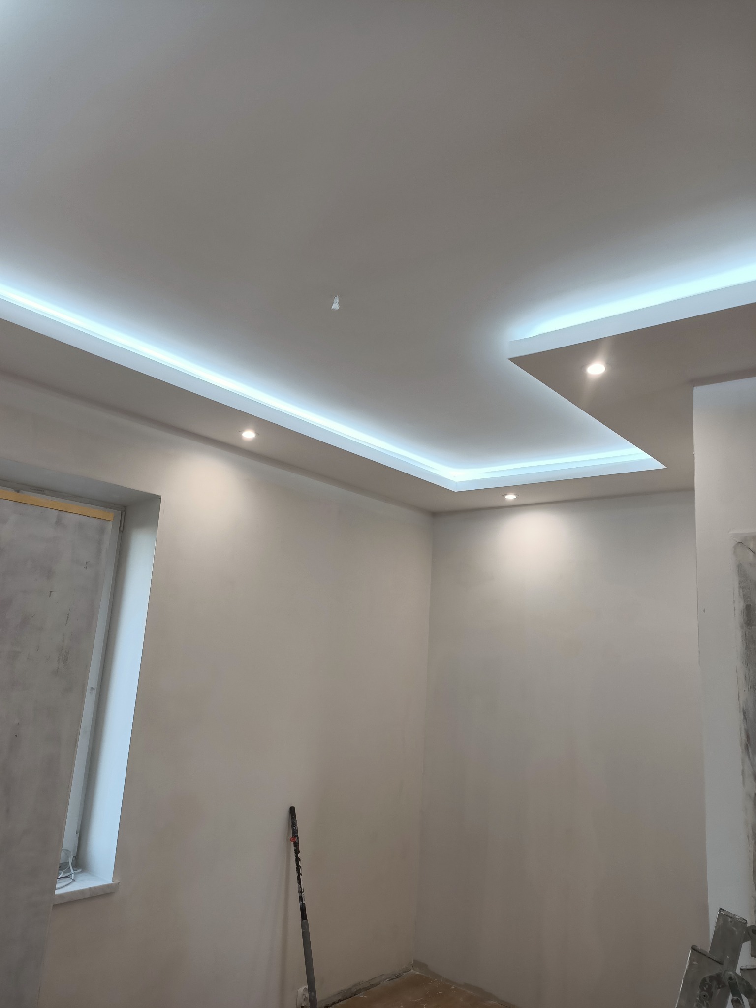Nowoczesny sufit podwieszany z oświetleniem LED, w trakcie prac wykończeniowych, widoczne narzędzia malarskie przy ścianie.
