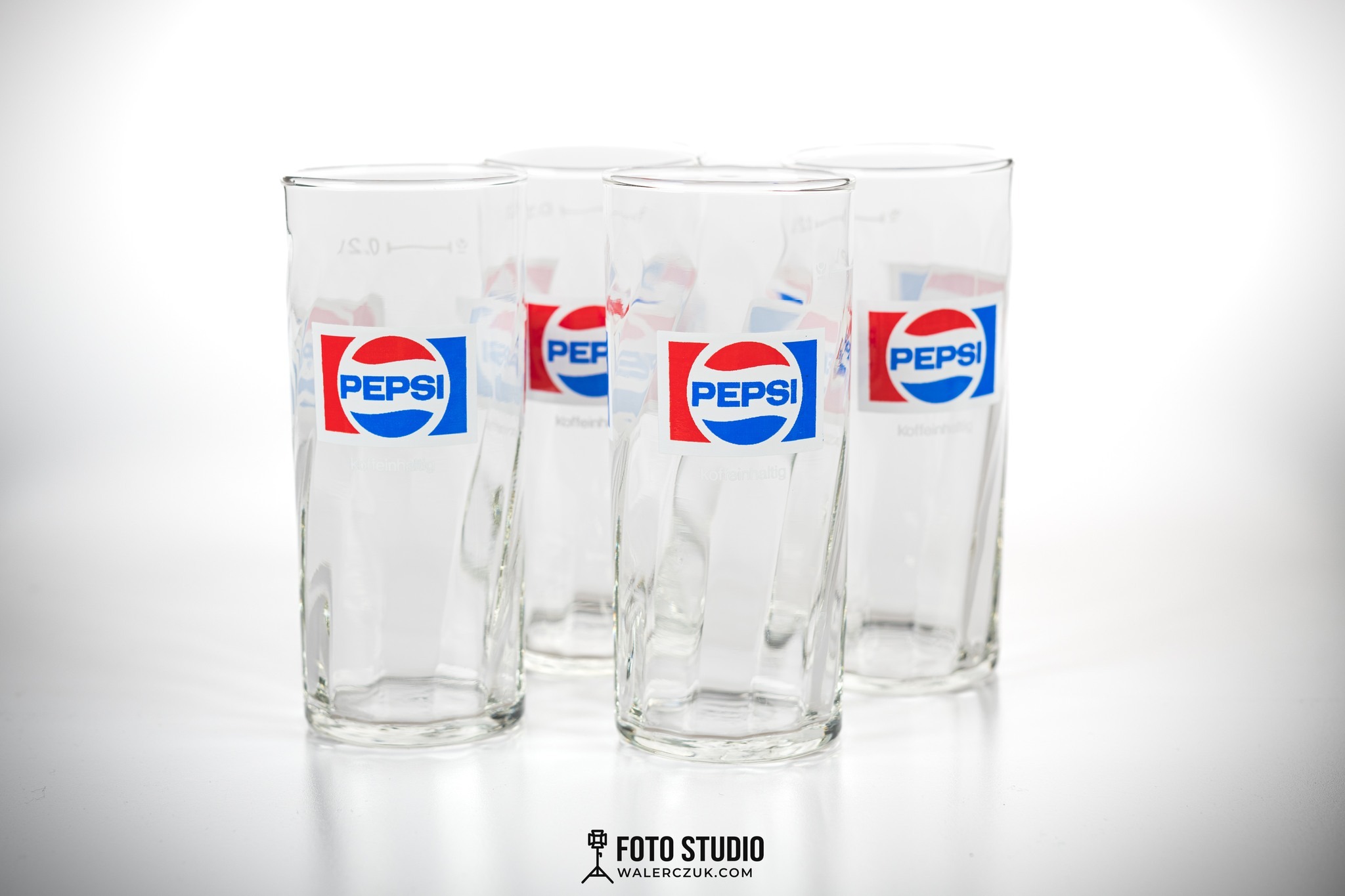 Cztery szklanki z logo Pepsi ustawione na białym, błyszczącym tle, sfotografowane w studiu.
