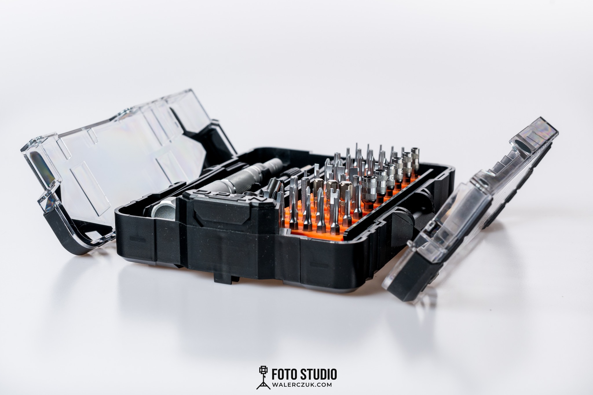 Otwarty zestaw bitów i wkrętaków w czarnym pudełku z pomarańczowym wnętrzem, wykonany w studio fotograficznym w Dobrczu, na białym tle.
