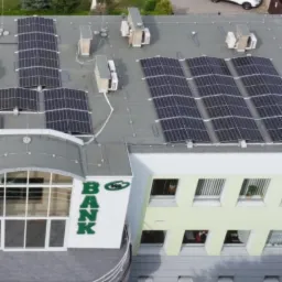 Widok z góry na budynek banku z zainstalowanymi panelami słonecznymi na dachu, obok zaparkowane samochody i budynek mieszkalny.