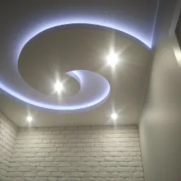 Nowoczesne wnętrze z podwieszanym sufitem w kształcie spirali, oświetlonym taśmą LED, oraz ścianą z białej cegły dekoracyjnej, oświetloną punktowymi lampami.