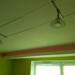 Dwa reflektory szynowe z przezroczystymi kloszami i żarówkami LED, zamontowane na suficie w pokoju z zielonymi ścianami i oknem.