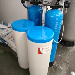 Zestaw urządzeń do filtracji wody: dwa niebieskie zbiorniki z wyświetlaczami oraz dwa białe pojemniki z niebieskimi pokrywami, obok worków z solą.