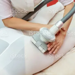 Kobieta w białym stroju poddawana zabiegowi na uda przy użyciu urządzenia z głowicą masującą i podciśnieniowym wężem