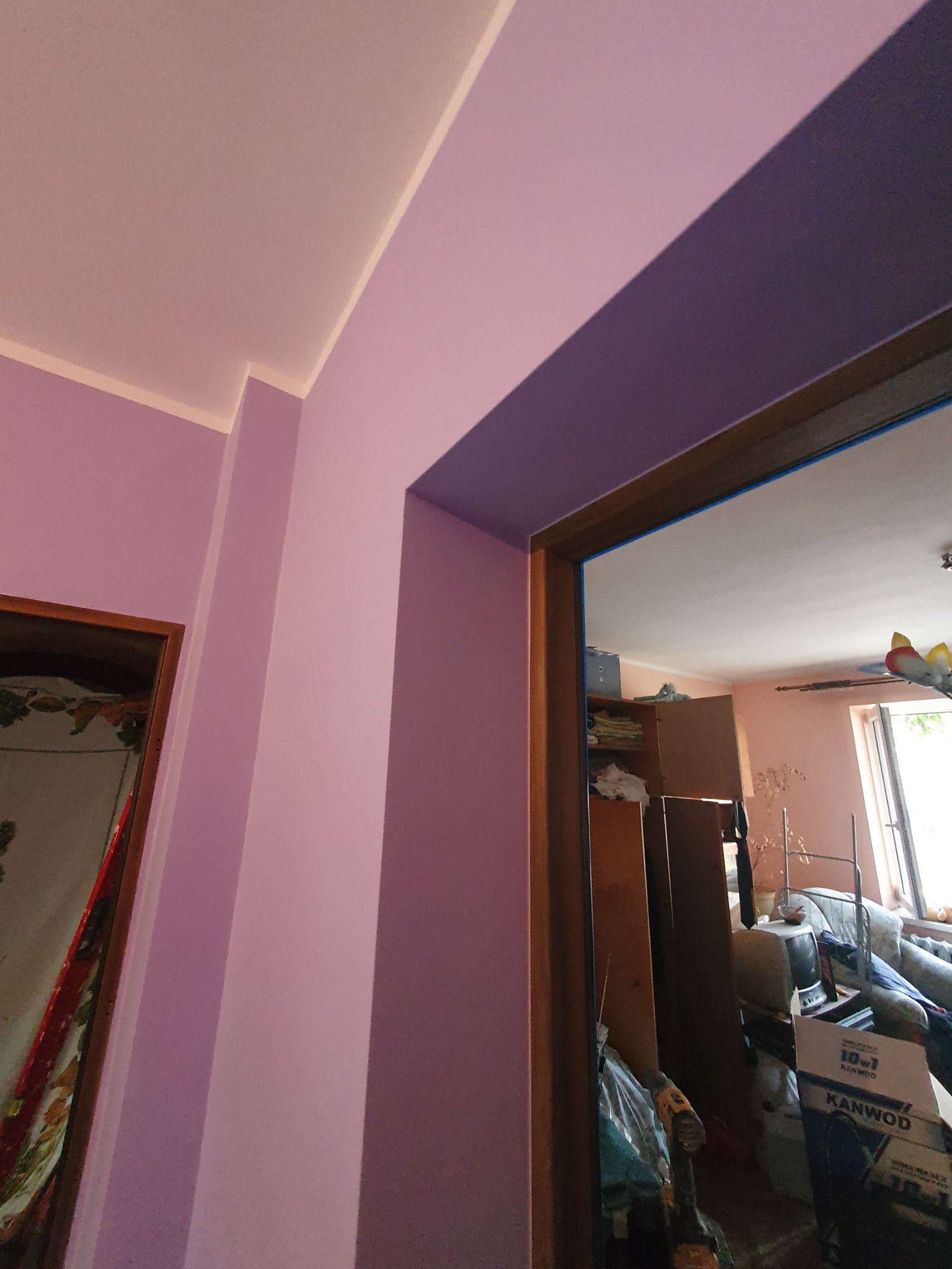 Świeżo pomalowane na liliowo ściany i futryna drzwiowa z widocznym nieporządkiem w tle remontowanego pomieszczenia.