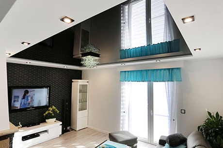 Elegancki salon z czarnym, lustrzanym sufitem podwieszanym, kryształowym żyrandolem, ścianą z ciemną, teksturowaną tapetą, telewizorem, białymi meblami i turkusowymi akcentami w oknach.