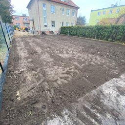 TomWer -Instalacje hydrauliczne, gazowe, wodne i kanalizacyjne, Usługi minikoparką Tomasz Kostuń - Przygotowany teren pod budowę z widocznymi śladami opon i pracującą koparką w tle, ogrodzony siatką.