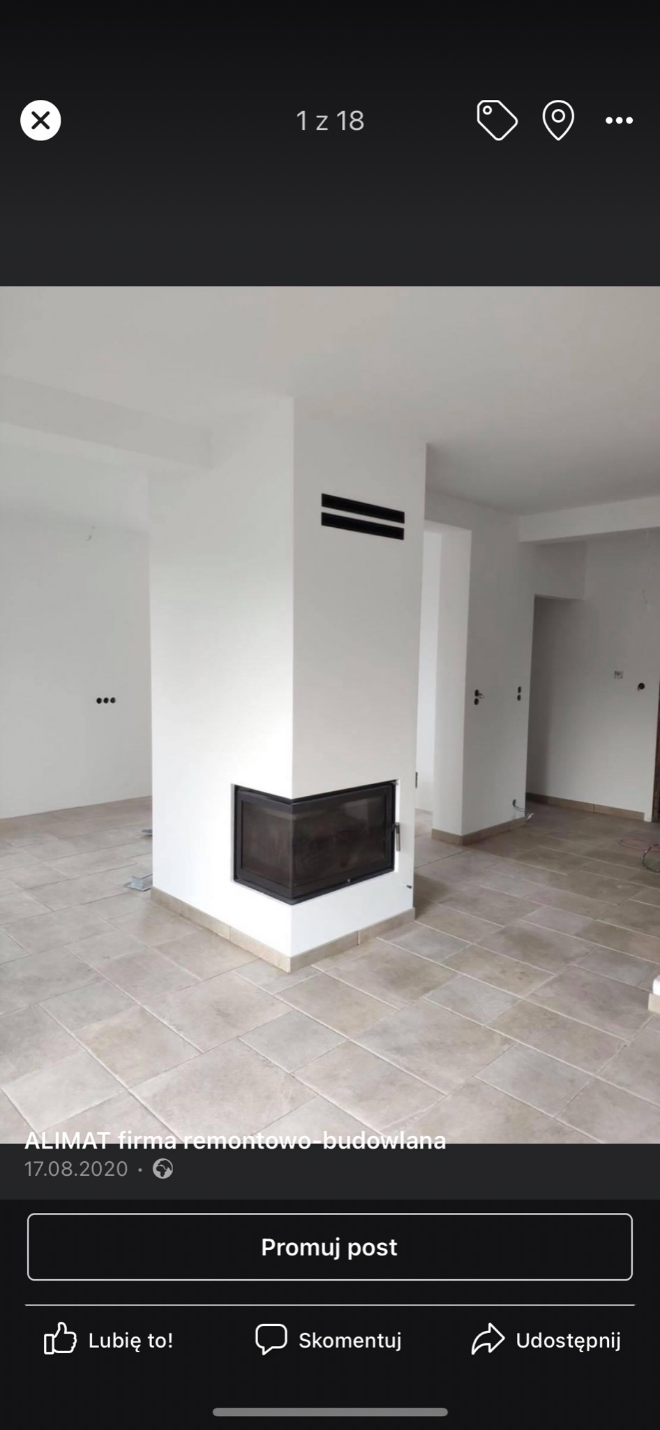 Wykończony pokój z jasnymi płytkami podłogowymi i nowoczesnym kominkiem narożnym z czarną ramą, w tle widoczne fragmenty ścian i sufitu pomalowane na biało.