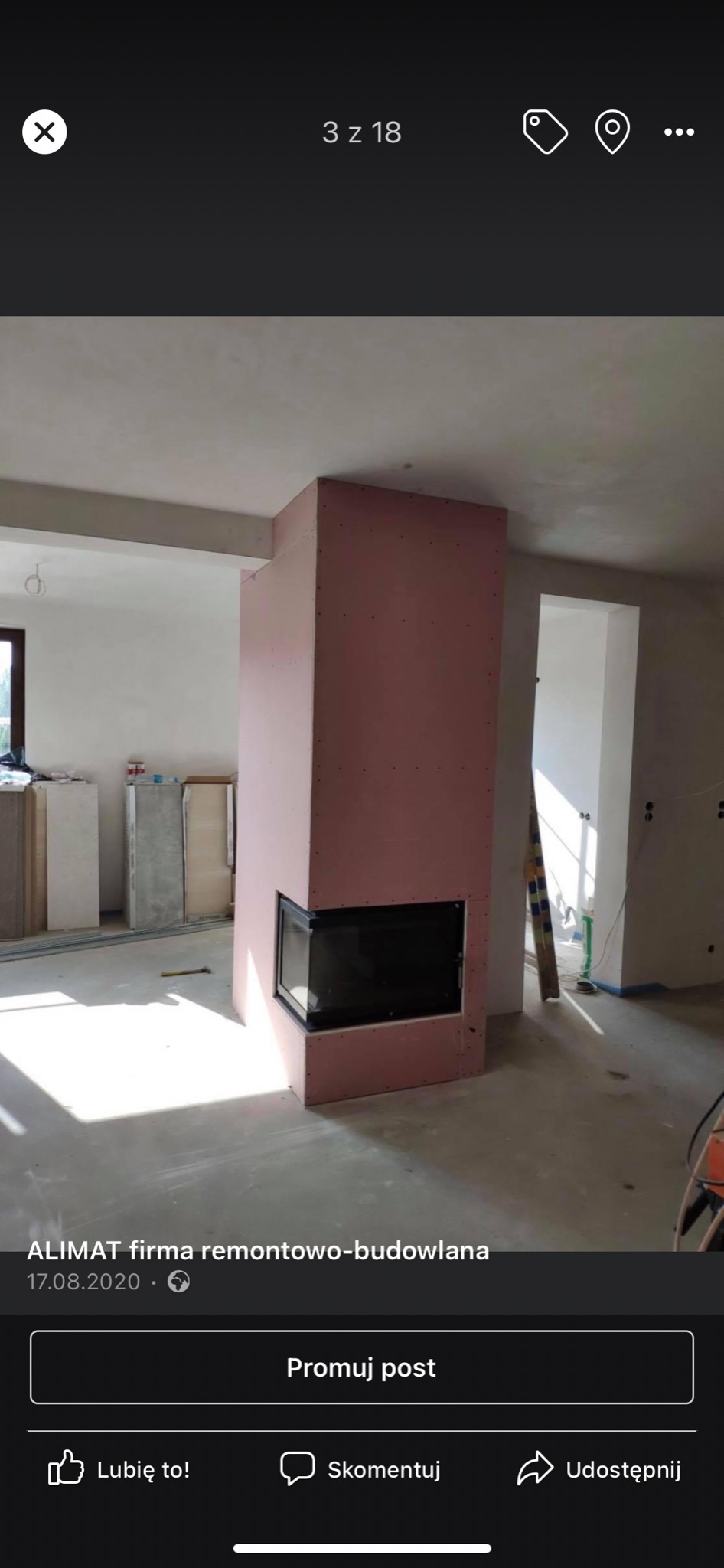 Wnętrze w trakcie remontu, widoczna obudowa kominka z płyt kartonowo-gipsowych, z zamontowanym wkładem kominkowym, surowy beton na podłodze, widoczne narzędzia i drabina w tle.