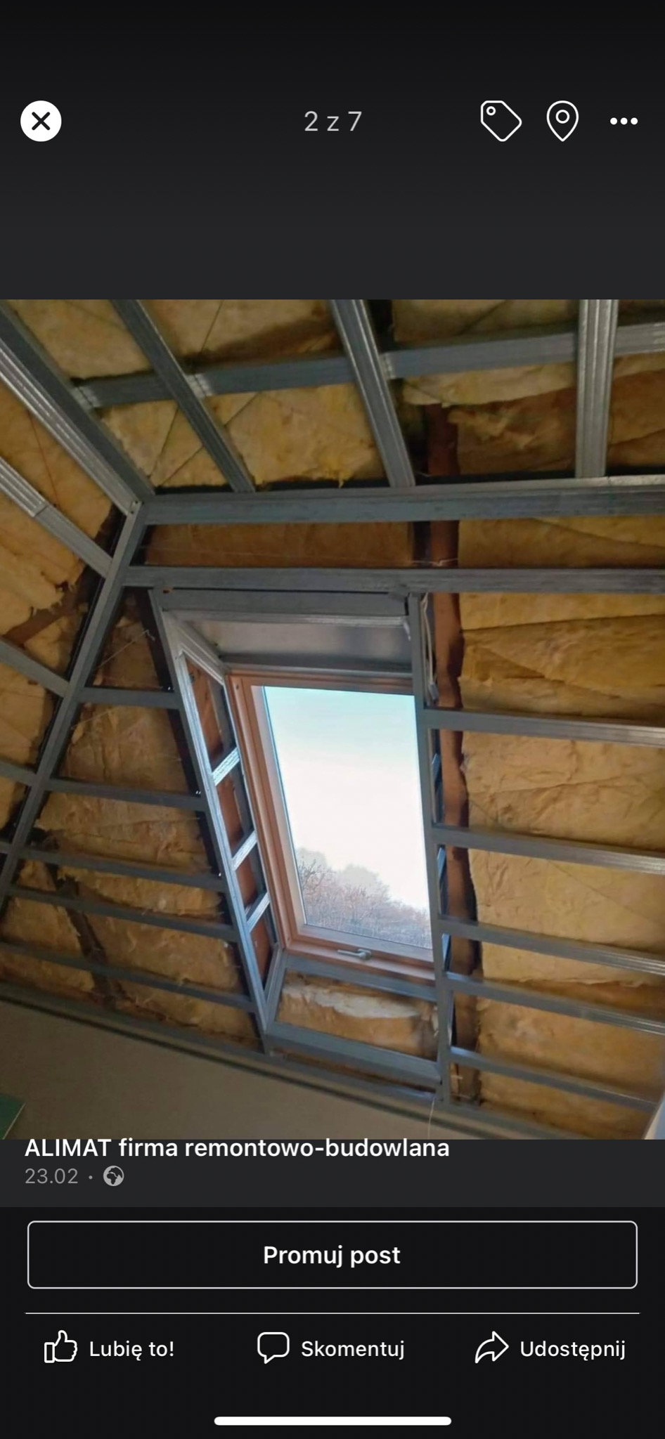 Skośny sufit poddasza w trakcie ocieplania wełną mineralną, widoczne metalowe profile pod płytę gipsowo-kartonową oraz okno dachowe z widokiem na drzewa.