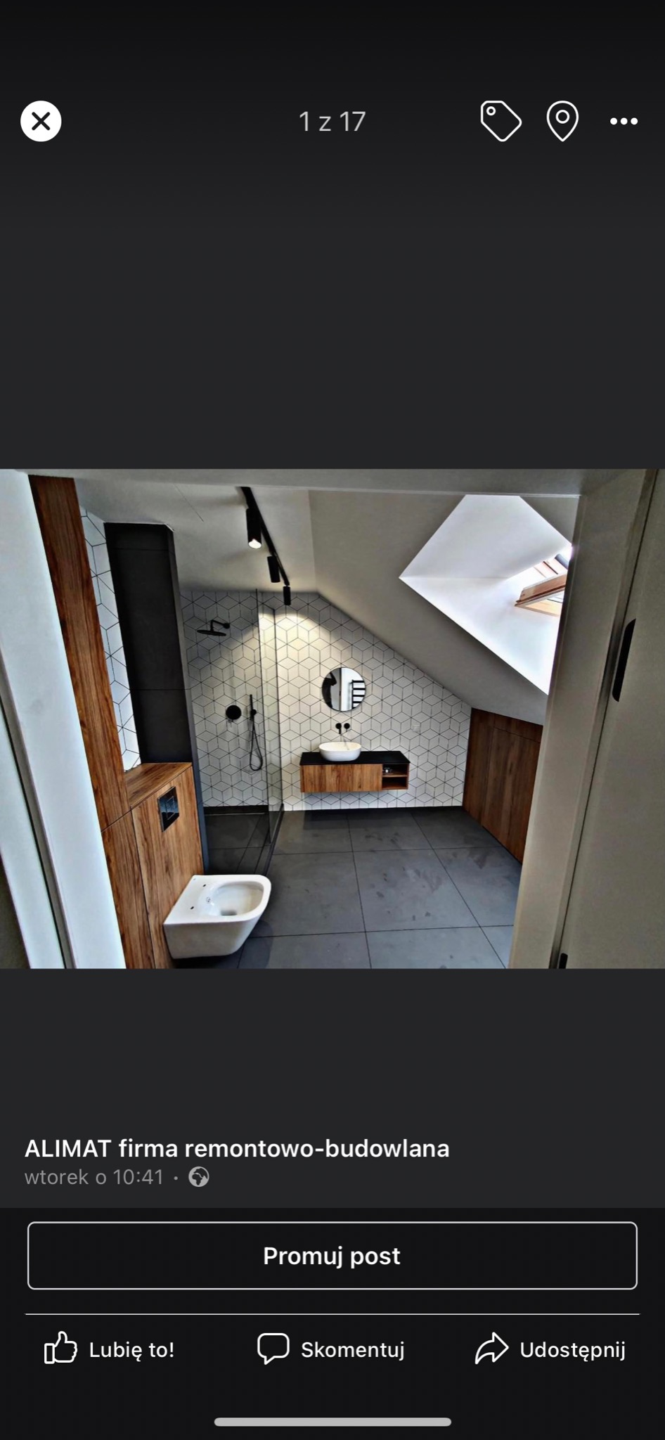 Nowoczesna łazienka na poddaszu ze skośnym sufitem, szare płytki podłogowe, biała wisząca toaleta, kabina prysznicowa ze szklaną ścianką, umywalka nablatowa na drewnianej szafce i okrągłe lustro...