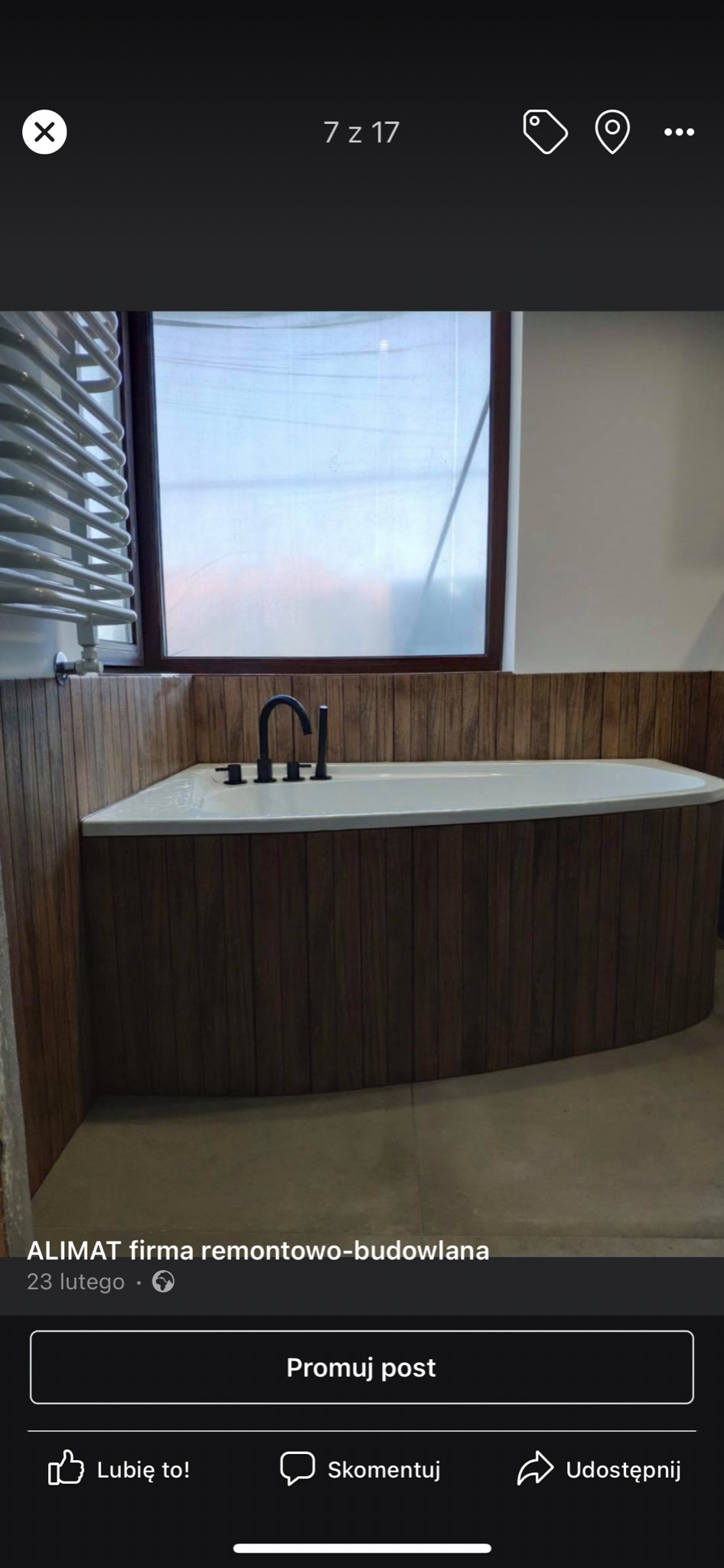 Nowoczesna wanna obudowana drewnianą boazerią z czarną armaturą w jasnej łazience z oknem.