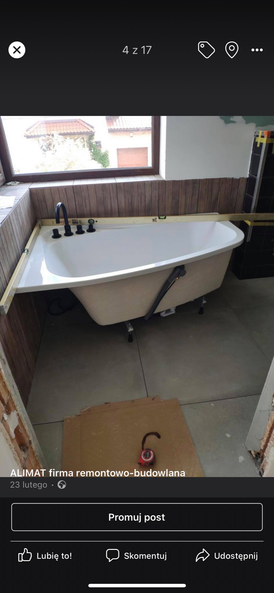 Montaż wanny z czarną armaturą w obudowie z paneli drewnopodobnych, poziomnica na krawędzi, widoczne płytki podłogowe i fragment ściany w trakcie prac wykończeniowych.