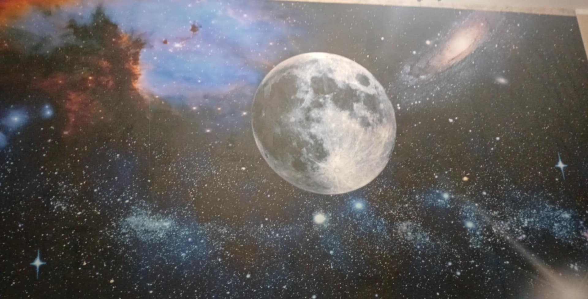 Kosmiczna tapeta z wyraźnym motywem księżyca, galaktyk i mgławic. Ciemne tło usiane gwiazdami, tworzy efekt głębi i przestrzeni. Dekoracja ścienna w pokoju.