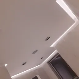 Nowoczesny sufit podwieszany z oświetleniem LED, widoczne otwory wentylacyjne i okno w tle, wykończenie w jasnych barwach.