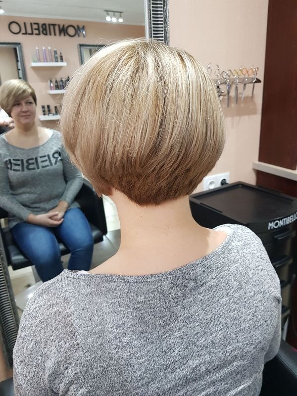 Krótkie, blond włosy po strzyżeniu bob, widok z tyłu na szyję klientki w szarej bluzce na tle lustra salonu.