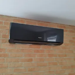 Czarna jednostka wewnętrzna klimatyzacji Gree Amber Standard zamontowana na ścianie z cegły dekoracyjnej w pomieszczeniu.