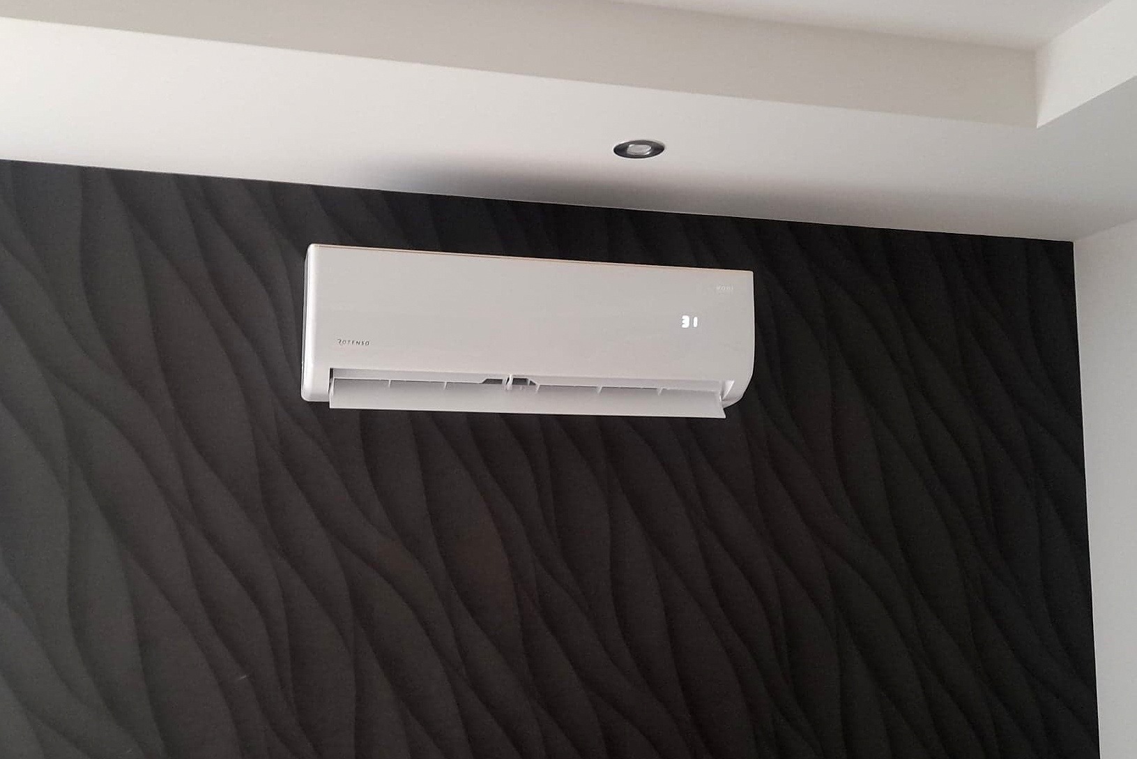 Biała klimatyzacja Rotenso Roni na ścianie z dekoracyjną, ciemną tapetą 3D, wyświetlająca temperaturę 31 stopni Celsjusza.