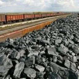 Stos czarnego węgla kamiennego na rampie kolejowej, z wagonami towarowymi w tle, widok z góry.