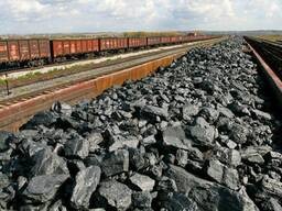 Stos czarnego węgla kamiennego na rampie kolejowej, z wagonami towarowymi w tle, widok z góry.