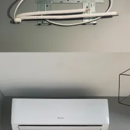 Montaż klimatyzatora: widoczna metalowa płyta montażowa na szarej ścianie z rurami, poniżej zamontowana biała jednostka wewnętrzna Gree, minimalistyczny design.