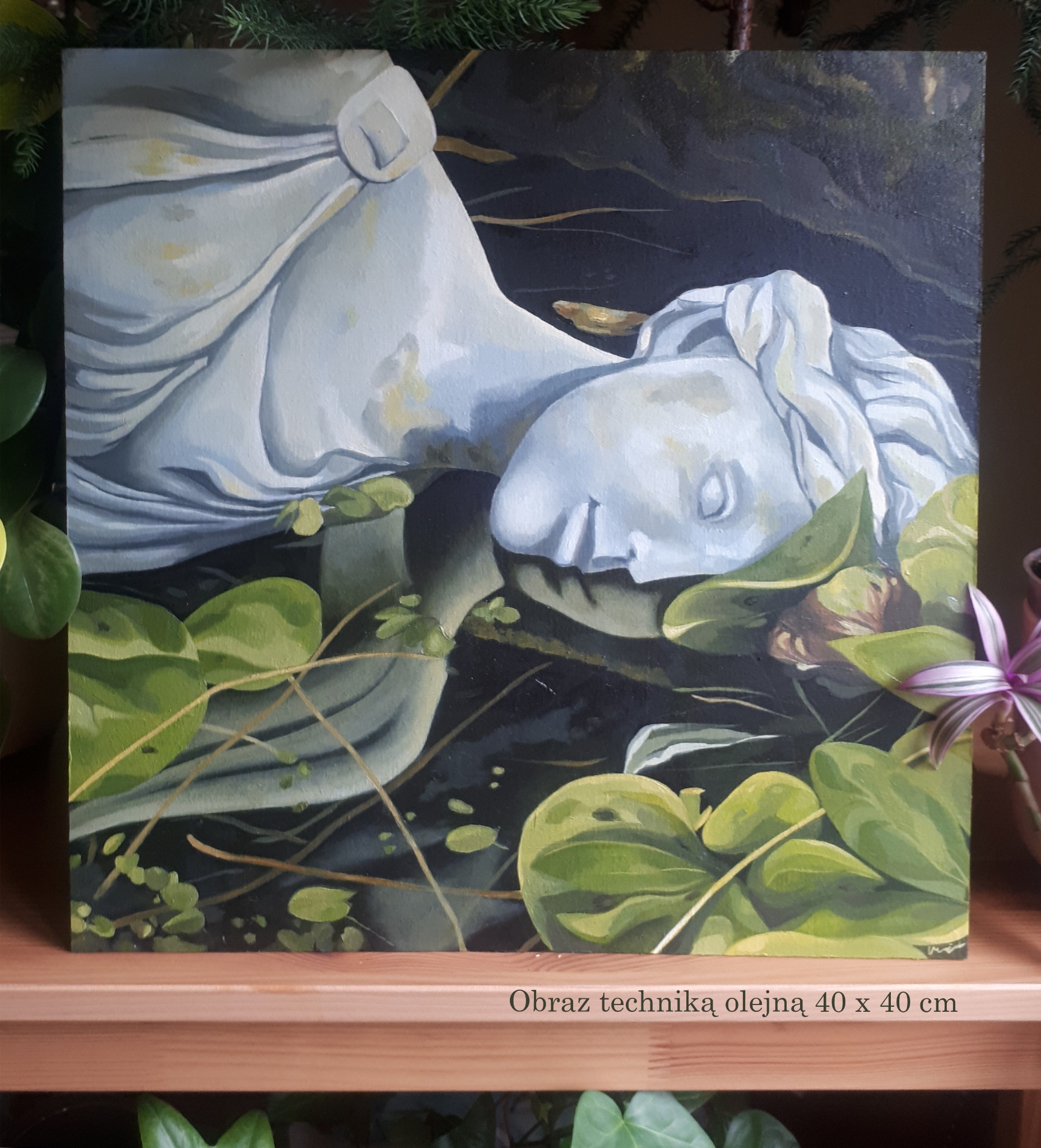 Obraz olejny 40x40 cm przedstawiający leżącą, białą rzeźbę kobiecą otoczoną liliami wodnymi na ciemnym tle, umieszczony na drewnianej półce.