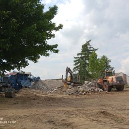 BARMEK - Plac budowy z koparką wyposażoną w młot hydrauliczny, ładowarką kołową oraz mobilną kruszarką do gruzu, przetwarzającą materiał na kruszywo.