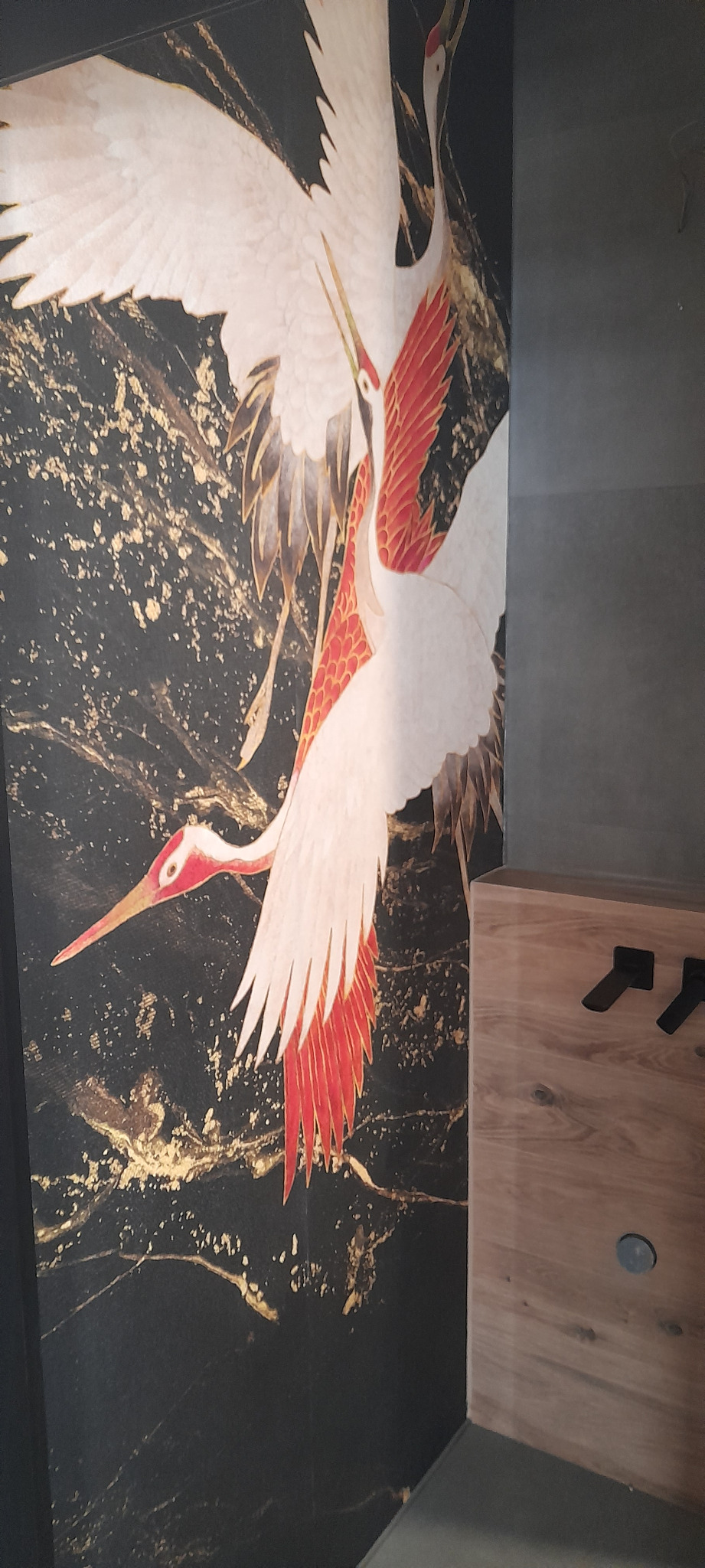 Tapeta z motywem dwóch żurawi na czarnym tle z złotymi żyłkami, obok drewniana zabudowa z czarnymi uchwytami.