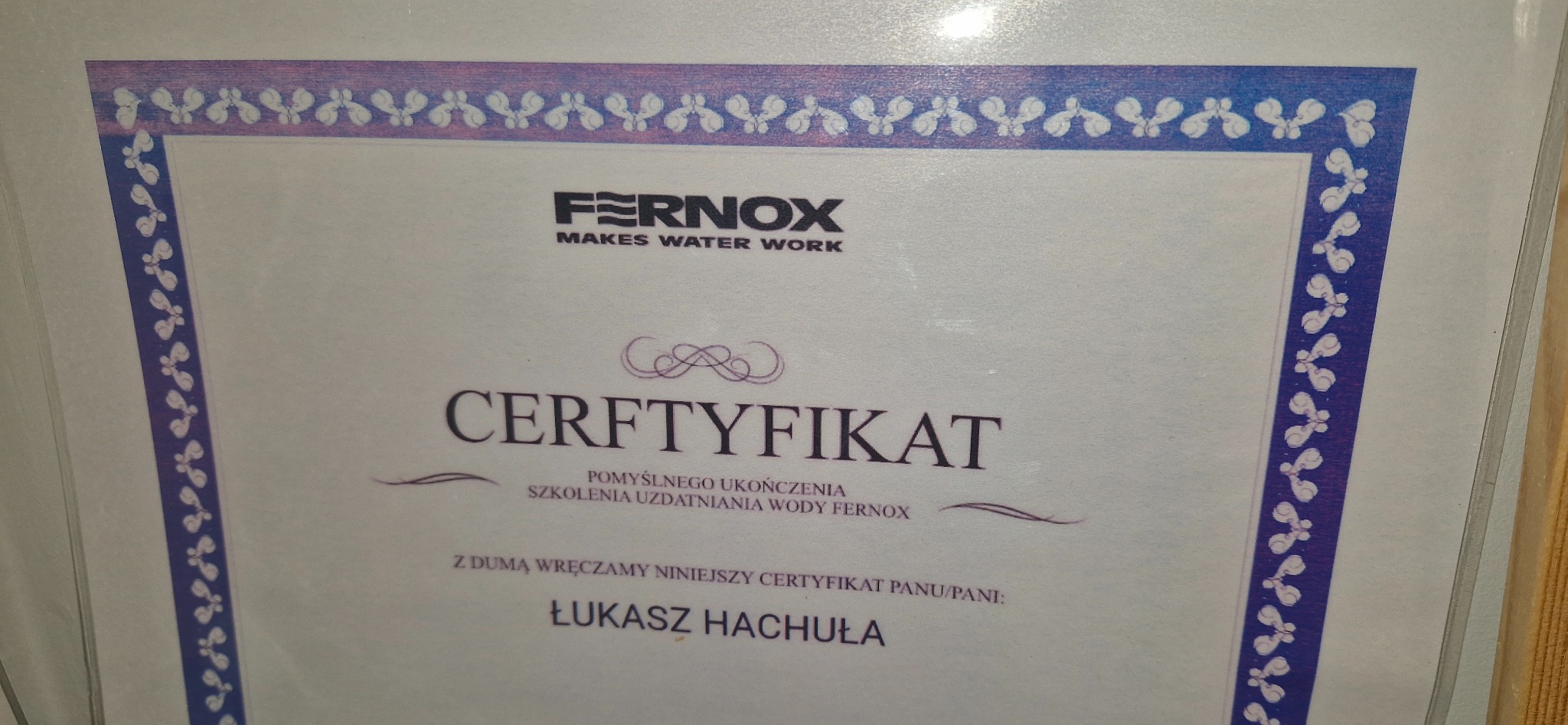 Certyfikat firmy Fernox za szkolenie uzdatniania wody dla Łukasza Hachuły, działającej w Bedoniu Przykościelnym, z ozdobną niebieską ramką.