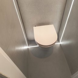 Trowelmaster - Nowoczesna toaleta w Ustroniu z oświetleniem LED wzdłuż ścian wykończonych w szarości, minimalistyczny design i czysta forma.