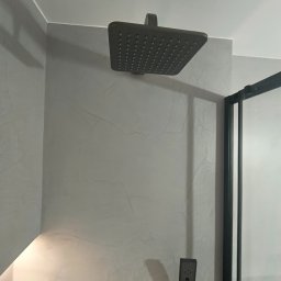 Trowelmaster - Nowoczesna łazienka z szarą ścianą wykończoną mikrocementem, deszczownicą i czarną kabiną prysznicową. Minimalistyczny design.
