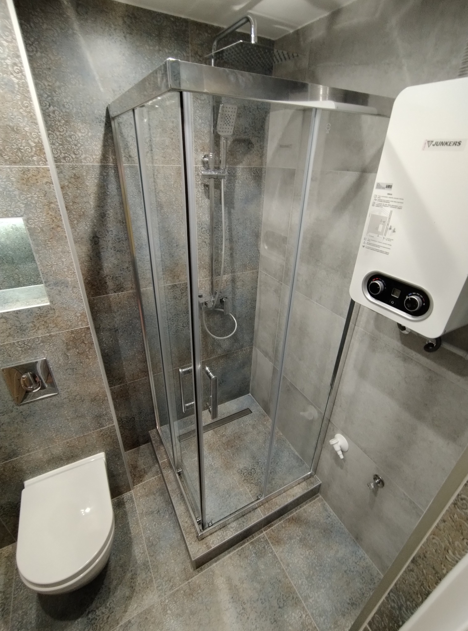 Szara łazienka z kabiną prysznicową z odpływem liniowym, wiszącą toaletą i bojlerem Junkers.