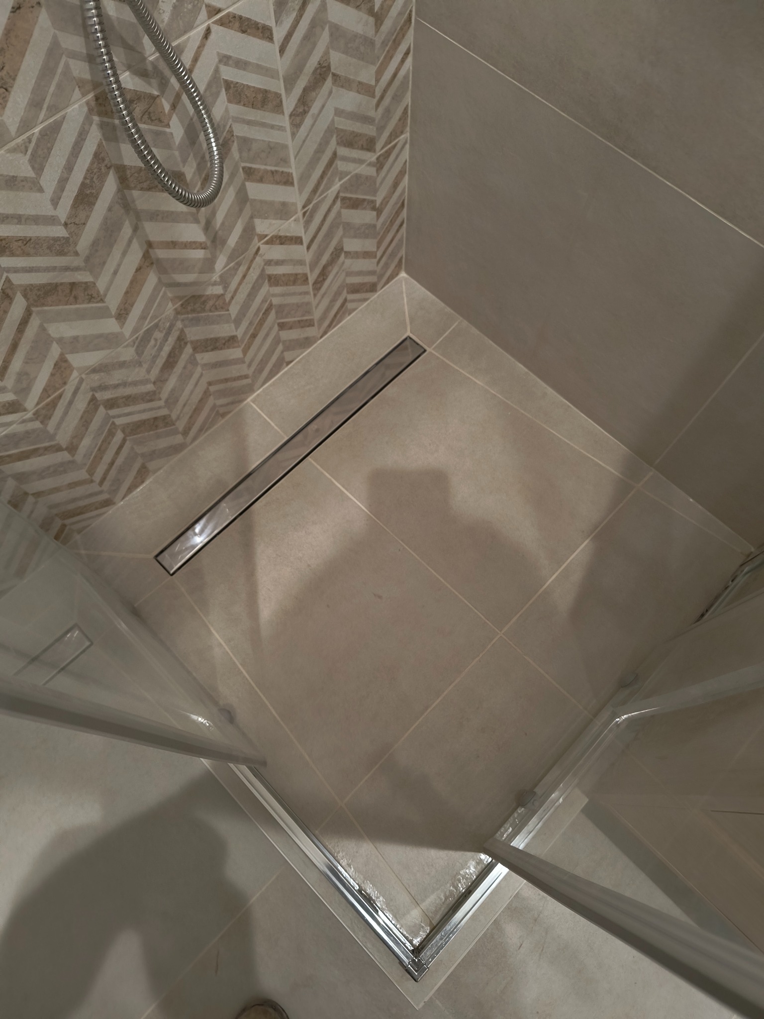 Wykończona kabina prysznicowa z odpływem liniowym i płytkami w odcieniach beżu, wzór jodełki na ścianie.