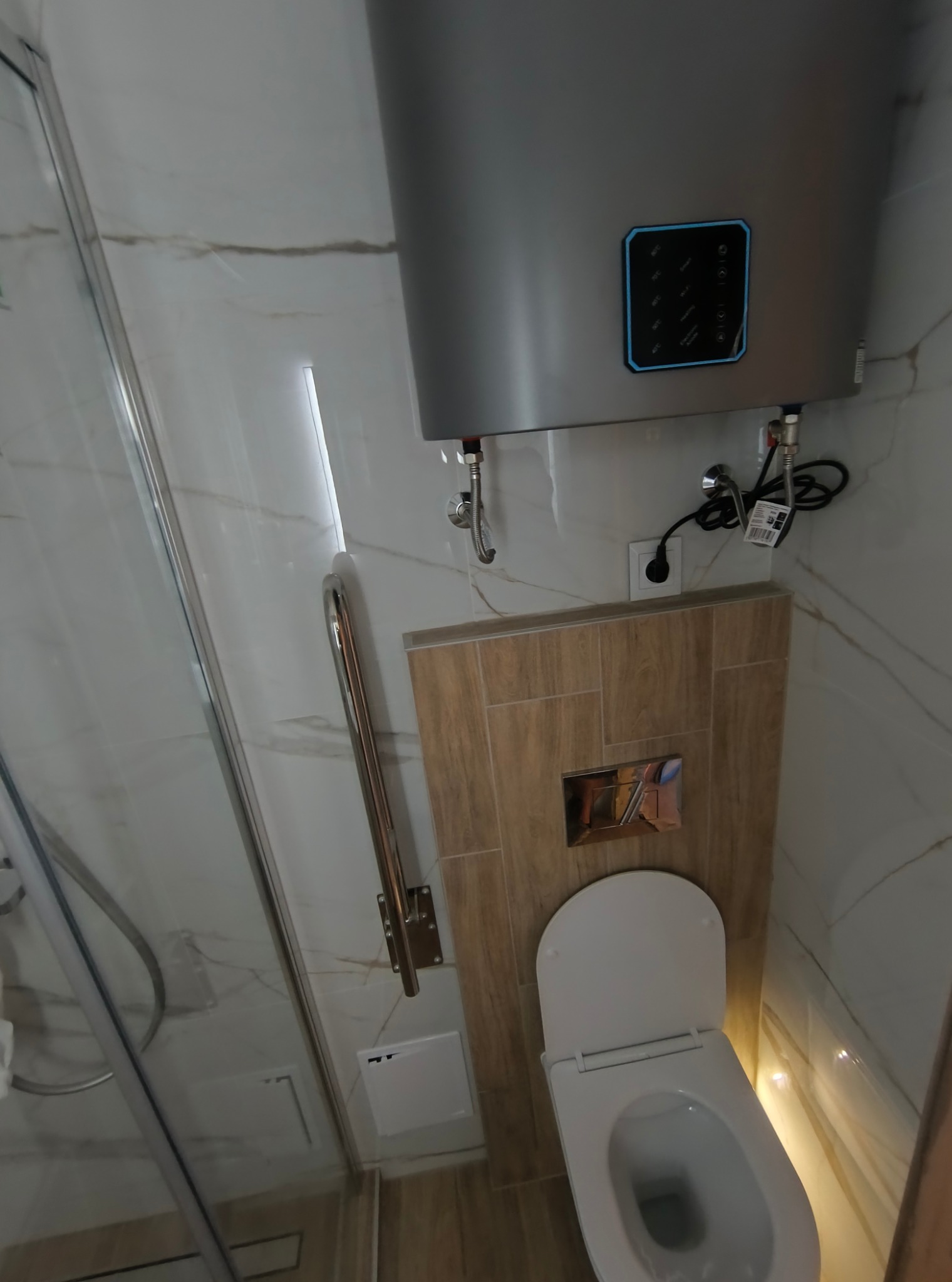 Nowoczesna łazienka z kabiną prysznicową, podwieszaną toaletą i grzejnikiem elektrycznym. Wykończenie w jasnych płytkach imitujących marmur.