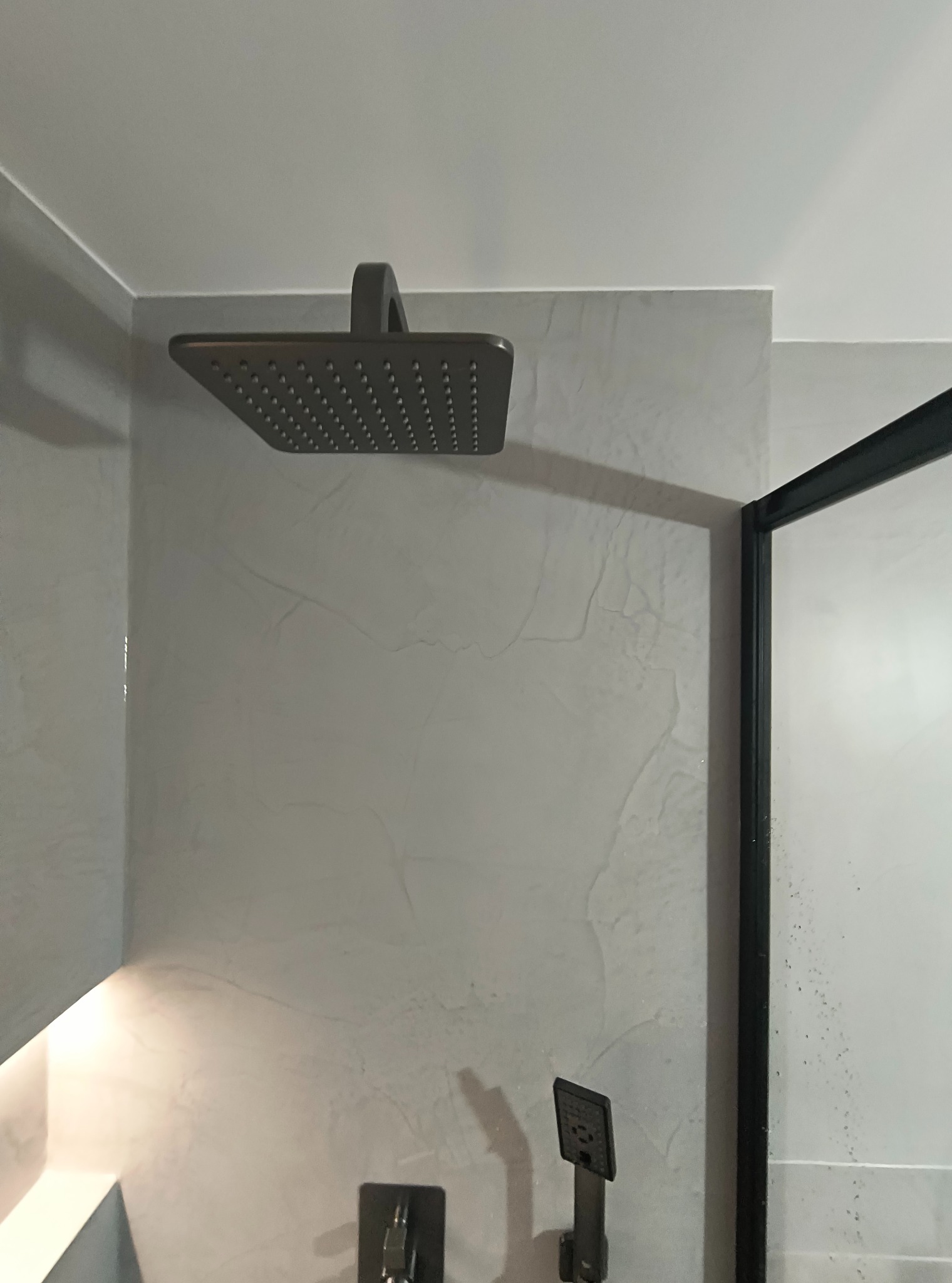 Nowoczesna kabina prysznicowa z deszczownicą i szarymi ścianami o fakturze imitującej kamień. Minimalistyczny design, czarne ramy kabiny.