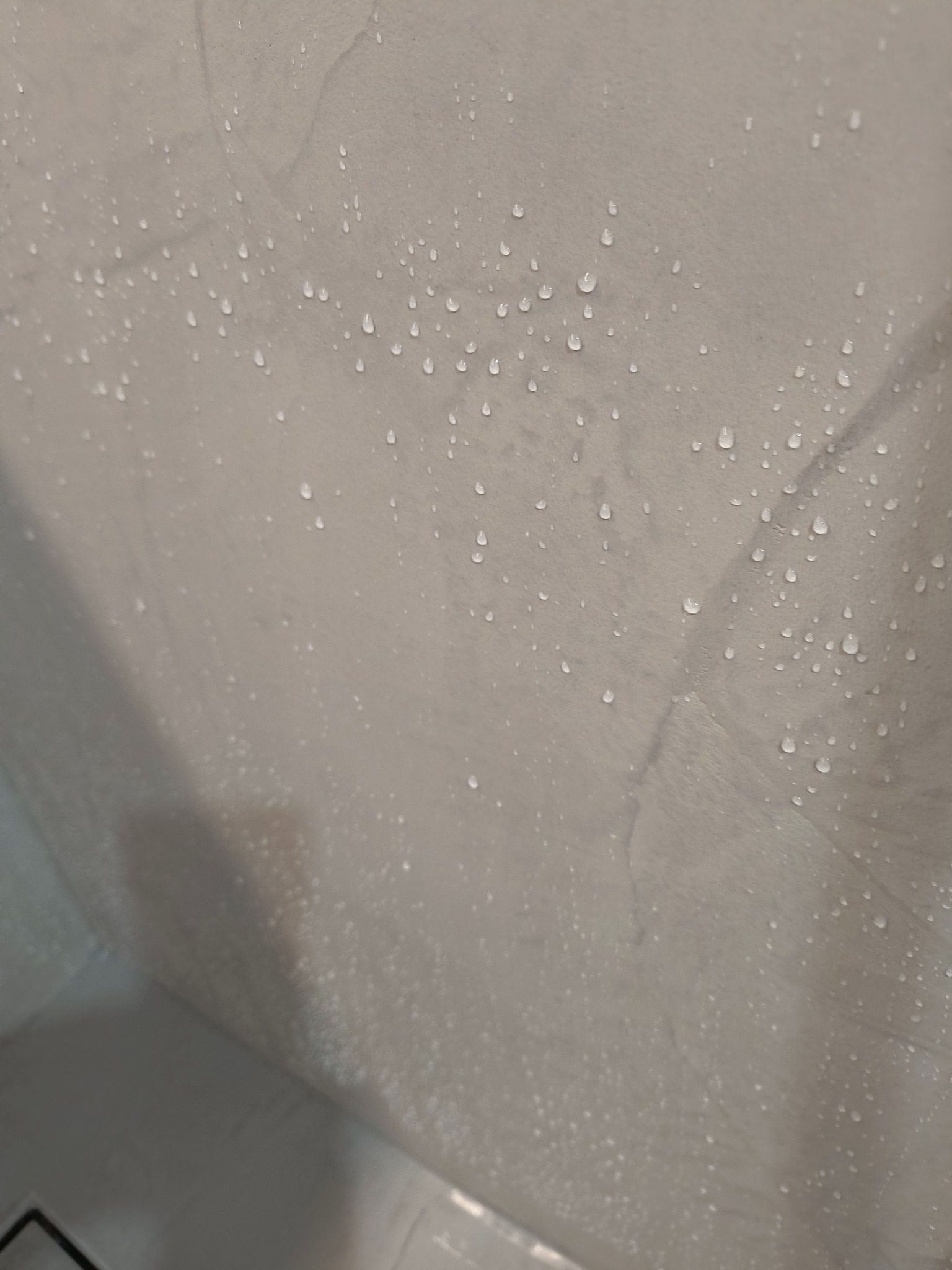 Ściana w łazience pokryta mikrocementem, na której osiadły krople wody. Widoczne delikatne wzory i faktura materiału. Minimalistyczny design.